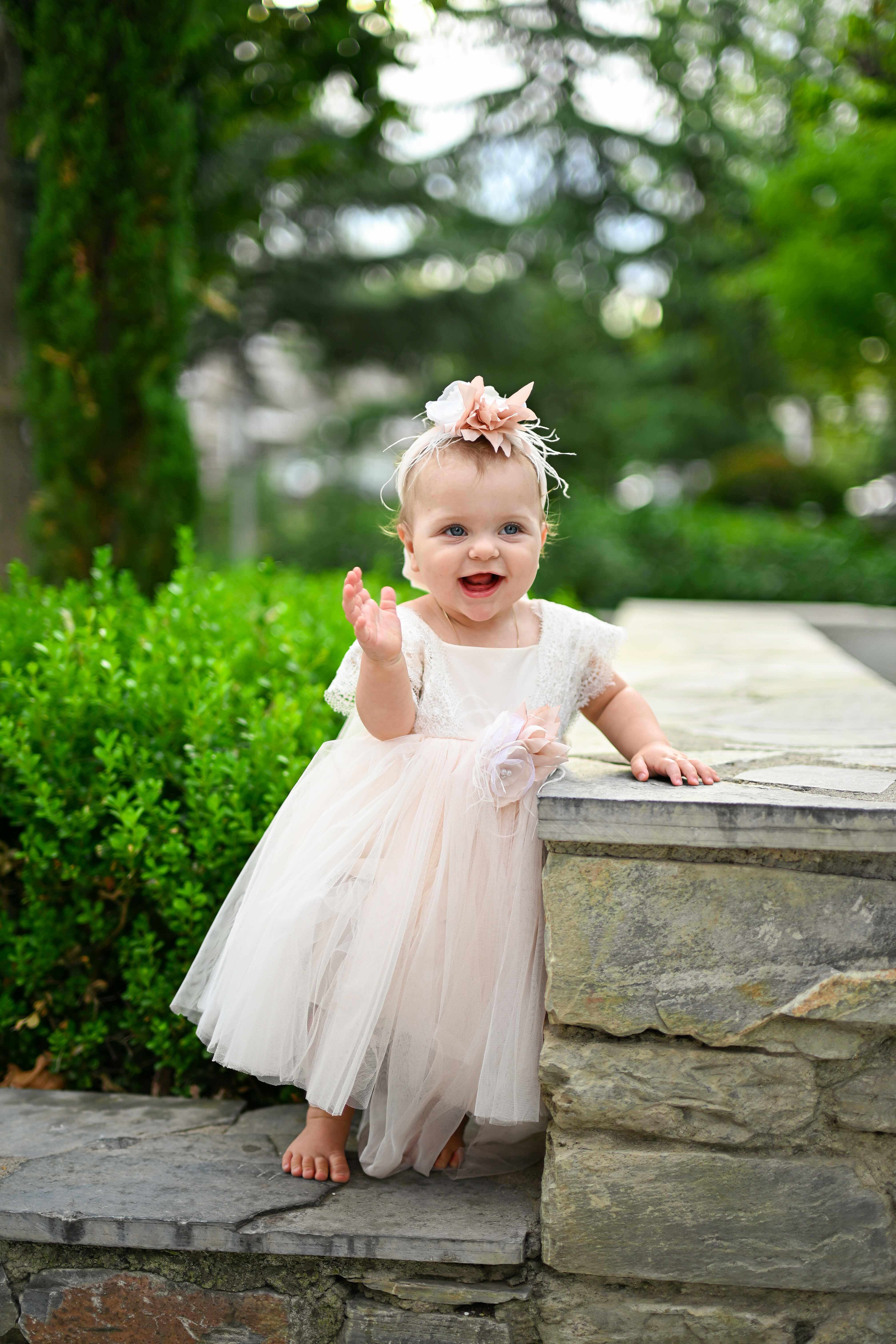 Κοριτσάκι με ροζ φόρεμα βάπτισης χαιρετάει σε κήπο - Φωτογραφείο Κολοβός